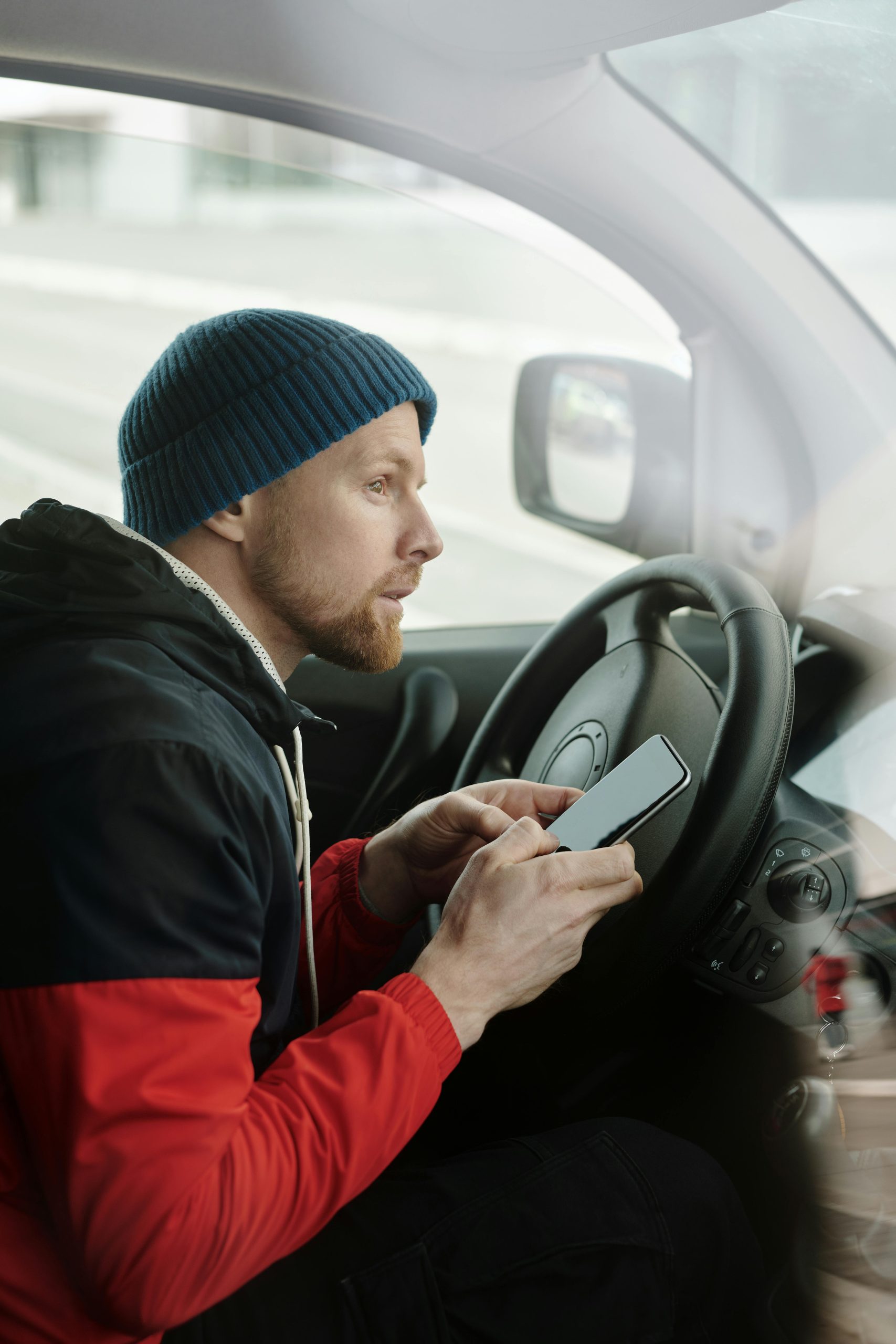 A man wearing a cap using a smartphone while sitting in a car, suggesting focused driving.