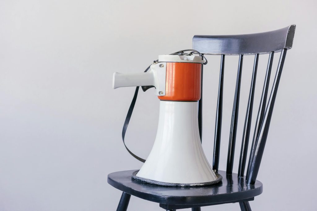 Close-up of a megaphone placed on a black wooden chair against a neutral background.