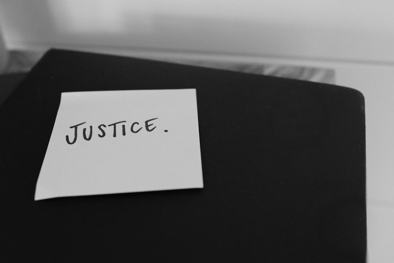 Black and white photo of a sticky note with 'Justice' written on it, conveying a powerful message.