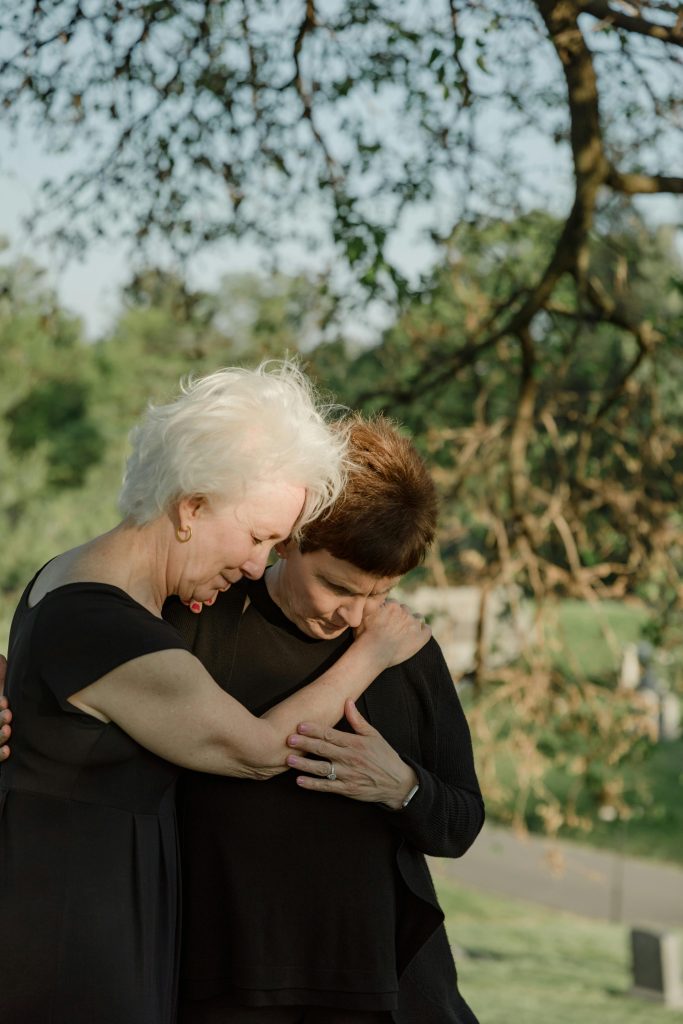 Two women embrace in a cemetery, symbolizing support and comfort in grief outdoors.