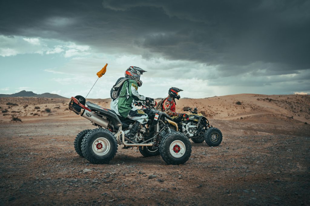 Two people riding ATVs in the Las Vegas desert under a dramatic sky.
