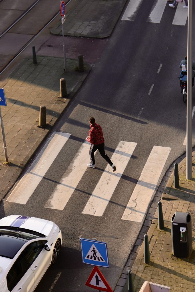 A person crossing a city street on a zebra crosswalk, viewed from above.